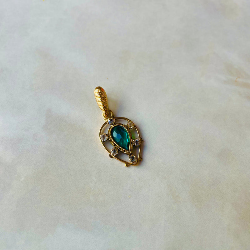 Gold pendant with a green gemstone on a light marble background | Deheb Jewellery Malta