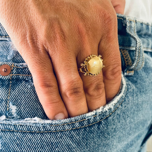 Hand wearing a gold ring with a large round centre worn by model