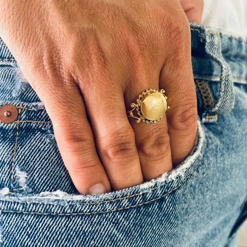 Hand wearing a gold ring with a large round centre worn by model