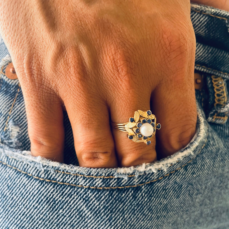 Gold ring with a central pearl and blue sapphires worn on model 