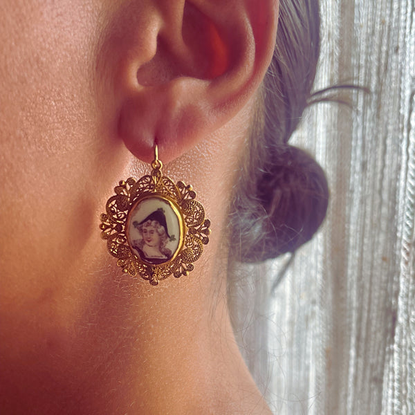 Gold earring with a portrait pendant worn by a person with a blurred background