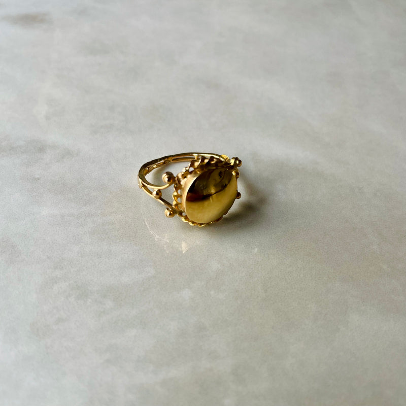 An antique gold ring with a high polished disc center set on a twisted band, placed on a marble surface.