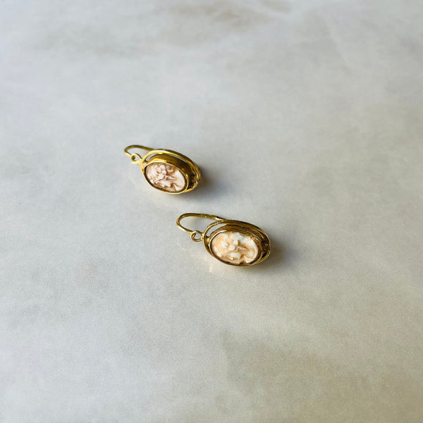Pair of gold earrings with a cameo on a light gray background