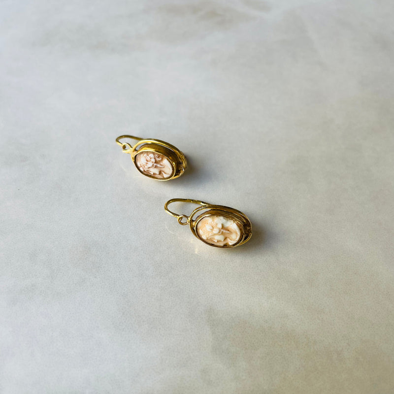 Pair of gold earrings with a cameo on a light gray background