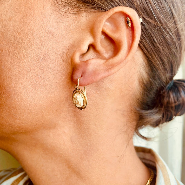 Close-up of a person wearing gold hoop earrings with a neutral background