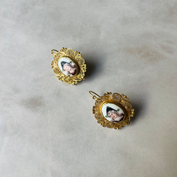 Gold filigree earrings with portrait designs on a light gray background