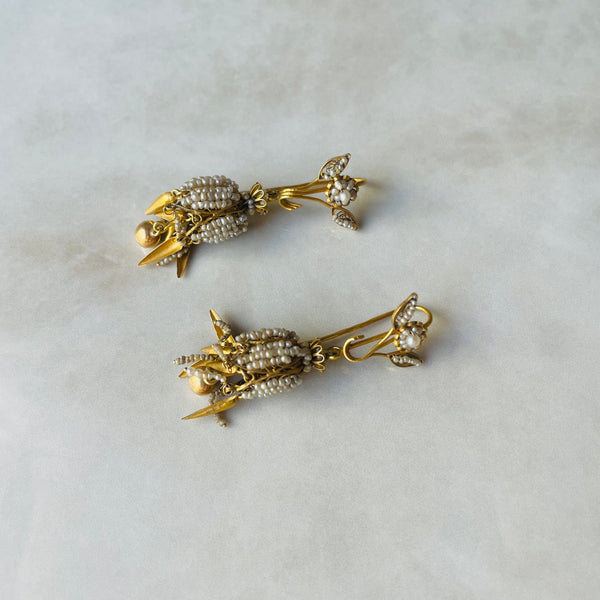 Pair of gold earrings with pearl-like stones on a light gray background