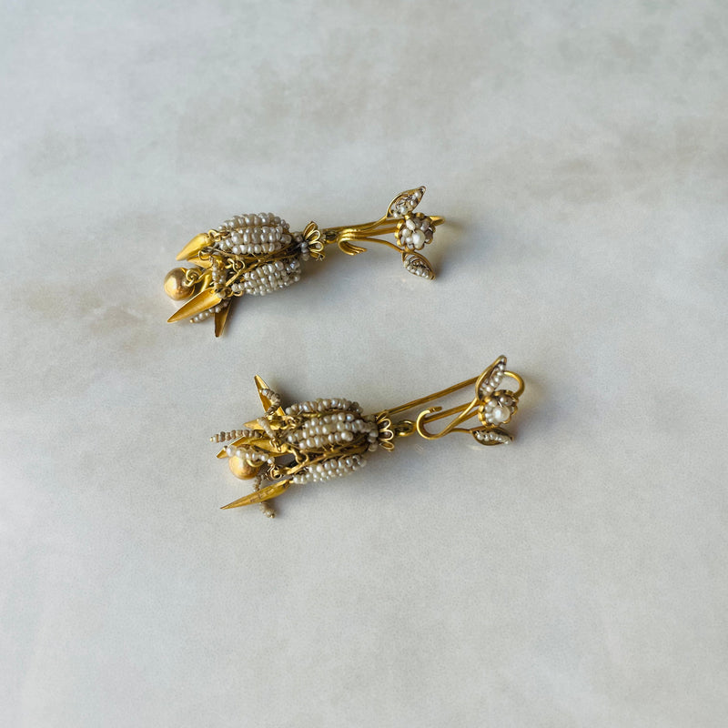 Pair of gold earrings with pearl-like stones on a light gray background