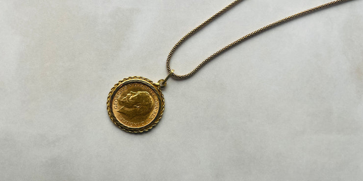 Gold coin pendant on a chain against a light gray background