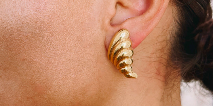 Gold spiral earring worn on an ear with a blurred background