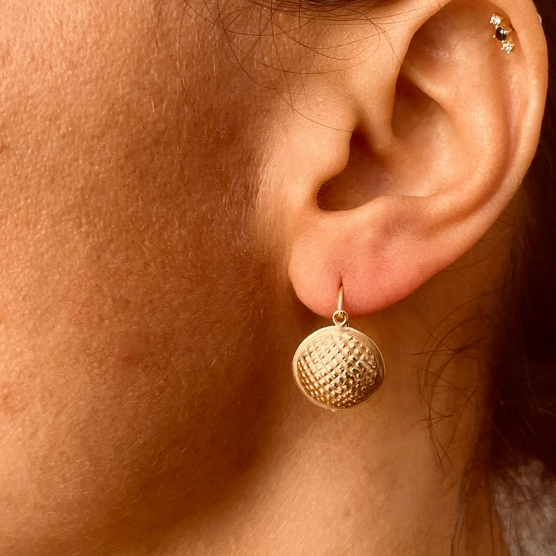 Close-up of a person wearing a gold textured disc earring | Deheb Malta Jewellery