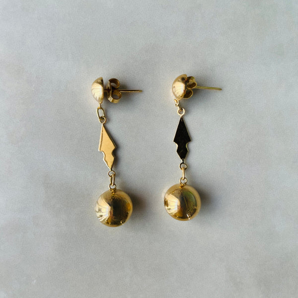 Pair of gold earrings with dangling elements on a gray background