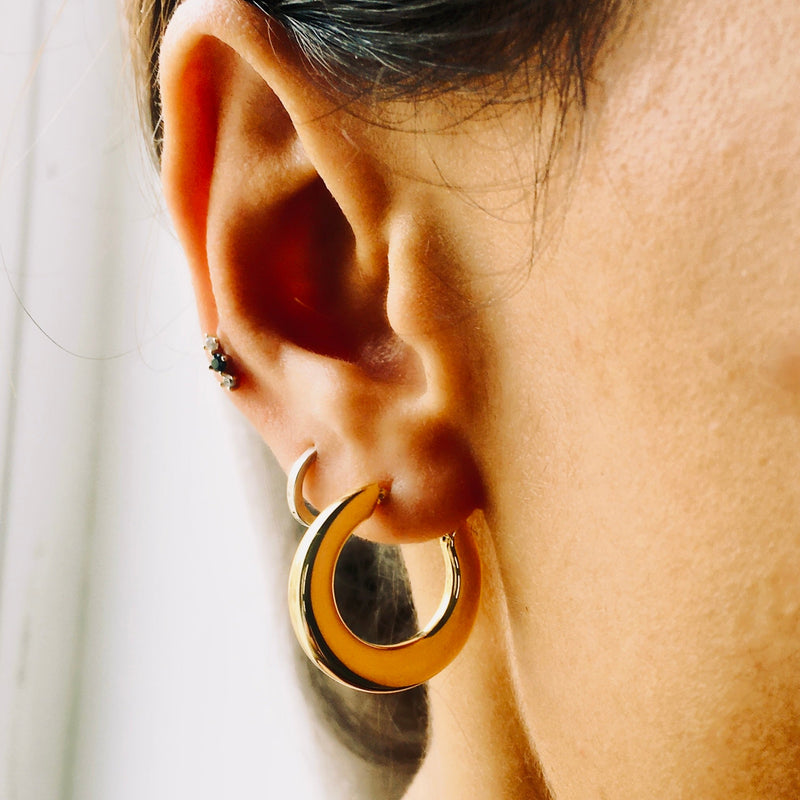 Close-up of a person wearing a gold hoop earring with a blurred background
