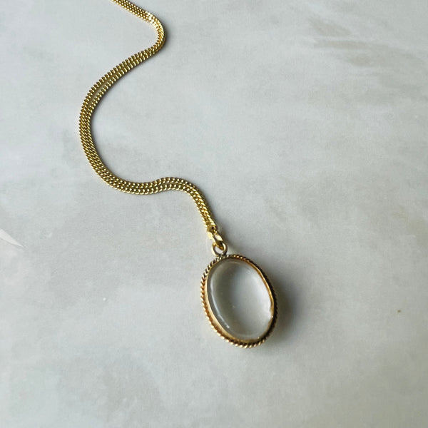 Gold necklace with a circular pendant on a light gray background