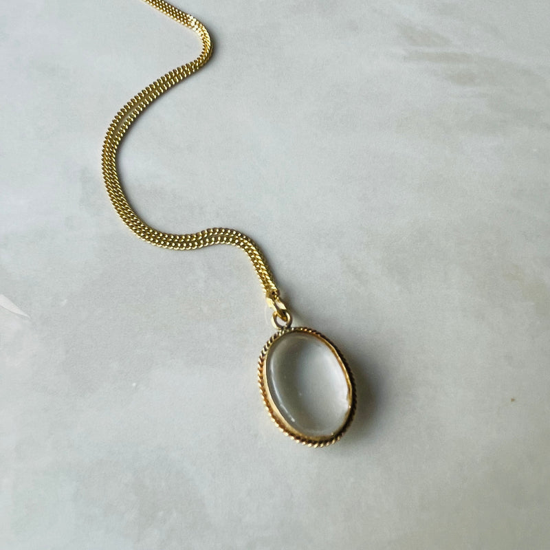 Gold necklace with a circular pendant on a light gray background