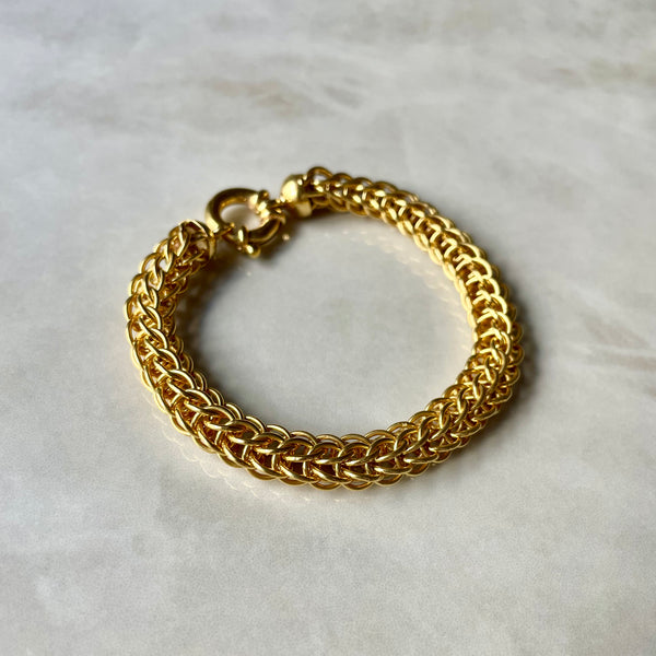 A gold interlocking-chain bracelet with a clasp, displayed on a marble surface.