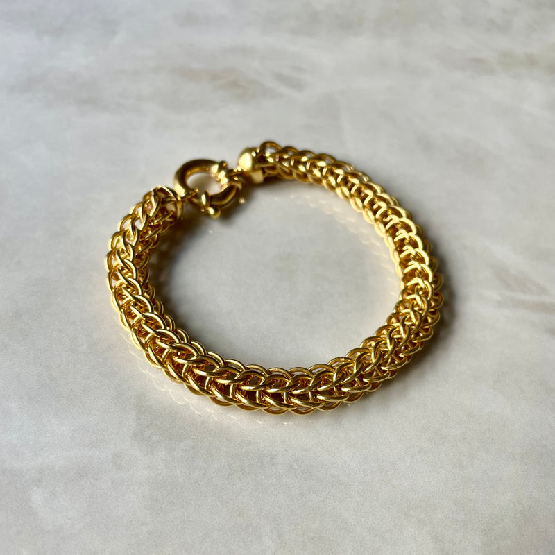 A gold interlocking-chain bracelet with a clasp, displayed on a marble surface.