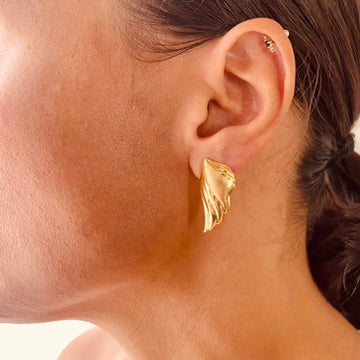 Gold earring worn by a person with a neutral background
