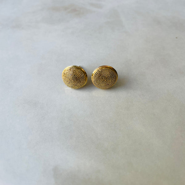 Pair of gold textured round earrings on a light gray background
