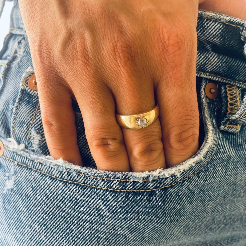 Hand wearing a gold ring with a diamond, peeking out from a blue denim pocket.