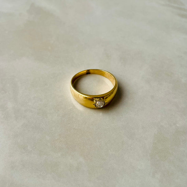 A single gold gypsy ring with a central old cut diamond, displayed on a marble surface.