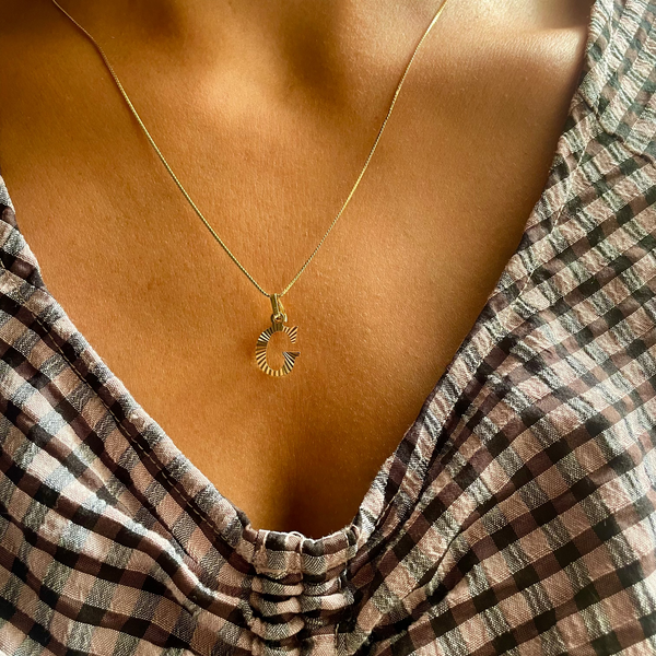 Gold necklace with a pendant worn by a person in a striped garment.