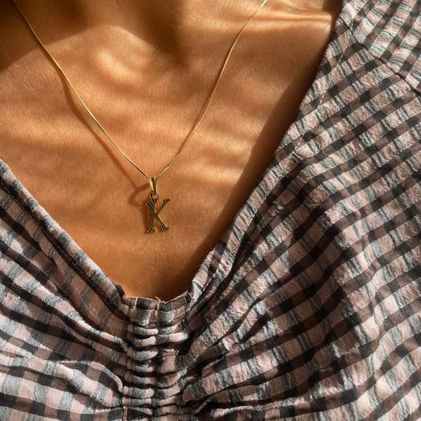Gold necklace with a pendant worn by a person in a plaid shirt.