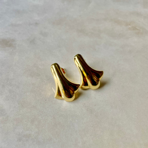 A pair of large, gold-colored stud earrings with a rippled design, displayed against a light background.