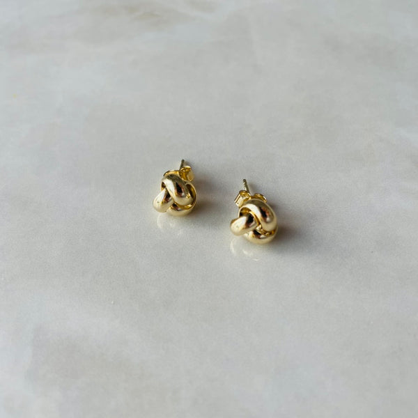 Pair of gold knot-shaped earrings on a light grey background | deheb Malta Jewellery
