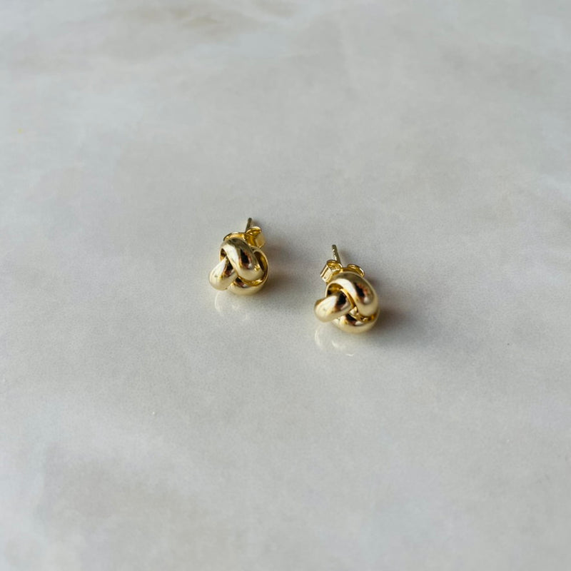 Pair of gold knot-shaped earrings on a light grey background | deheb Malta Jewellery