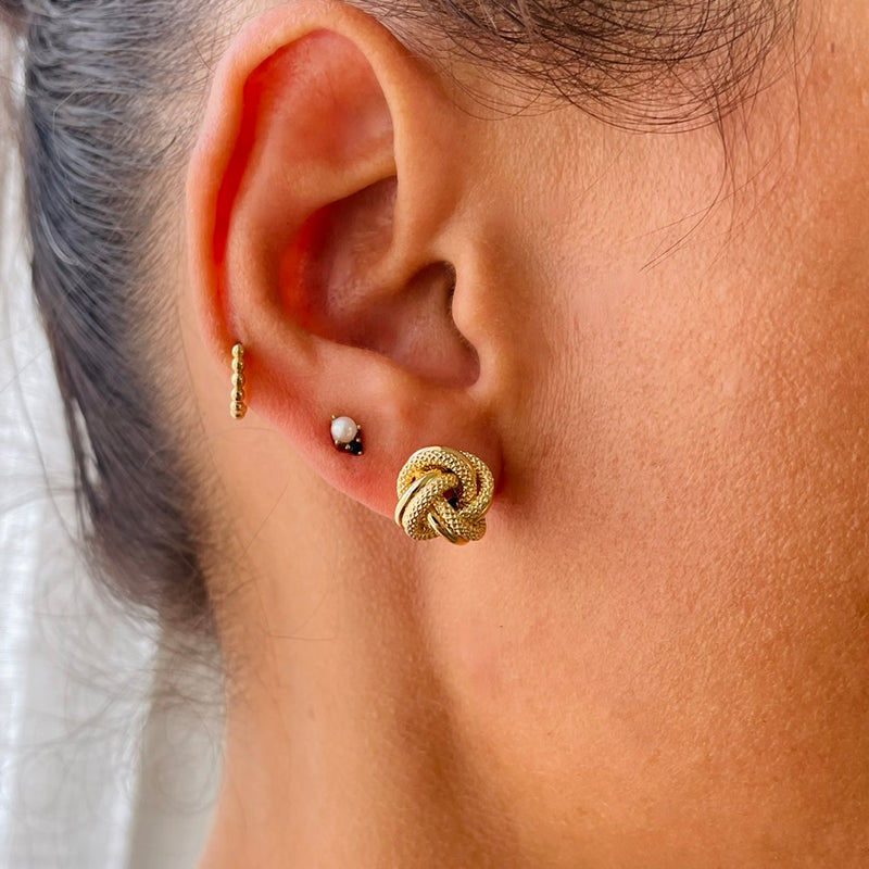 Close-up of an ear wearing a gold knot earring on model | Deheb Jewellery Malta