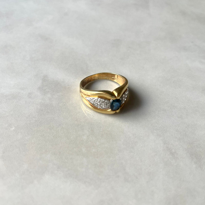 A gold ring with a large sapphire center stone and smaller diamond side stones on a white background.