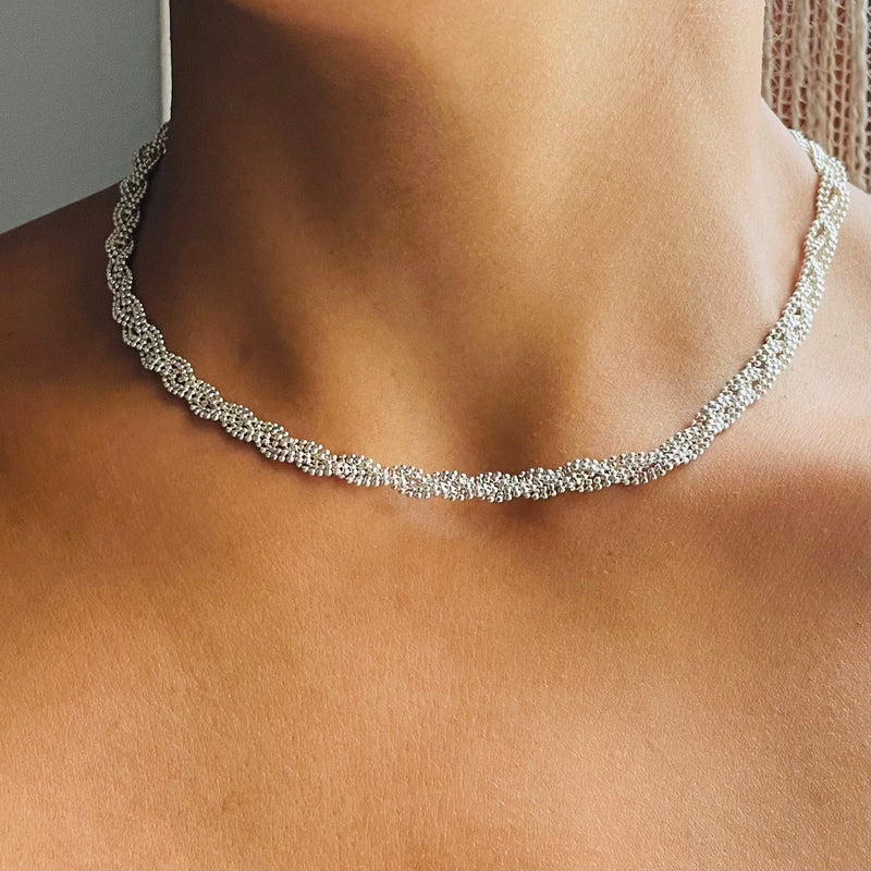 Silver necklace on a person's neck with a neutral background