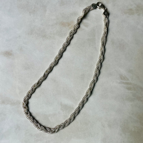 Silver braided necklace on a light gray background