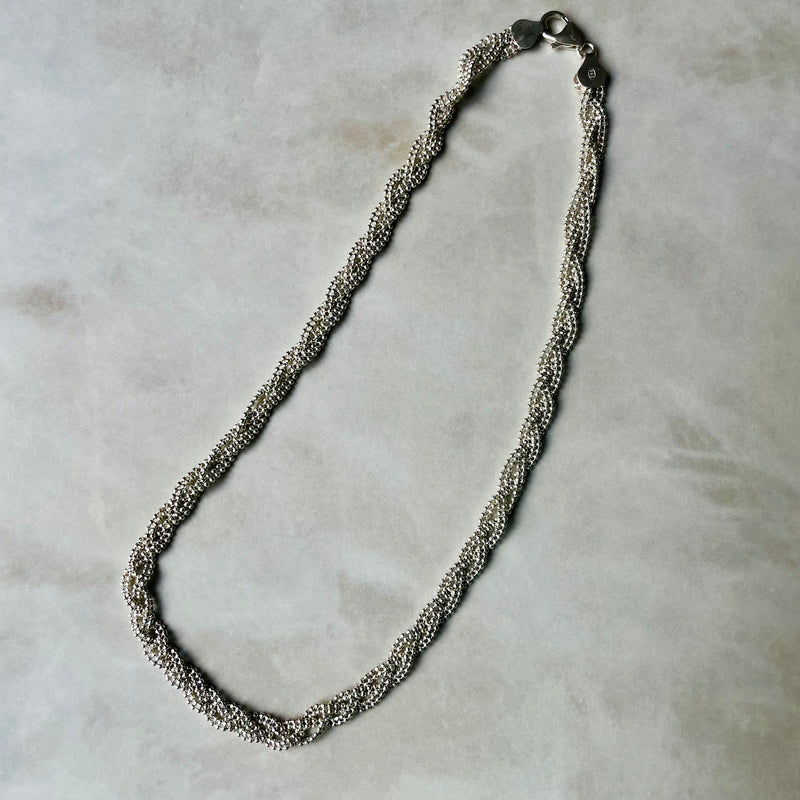Silver braided necklace on a light gray background