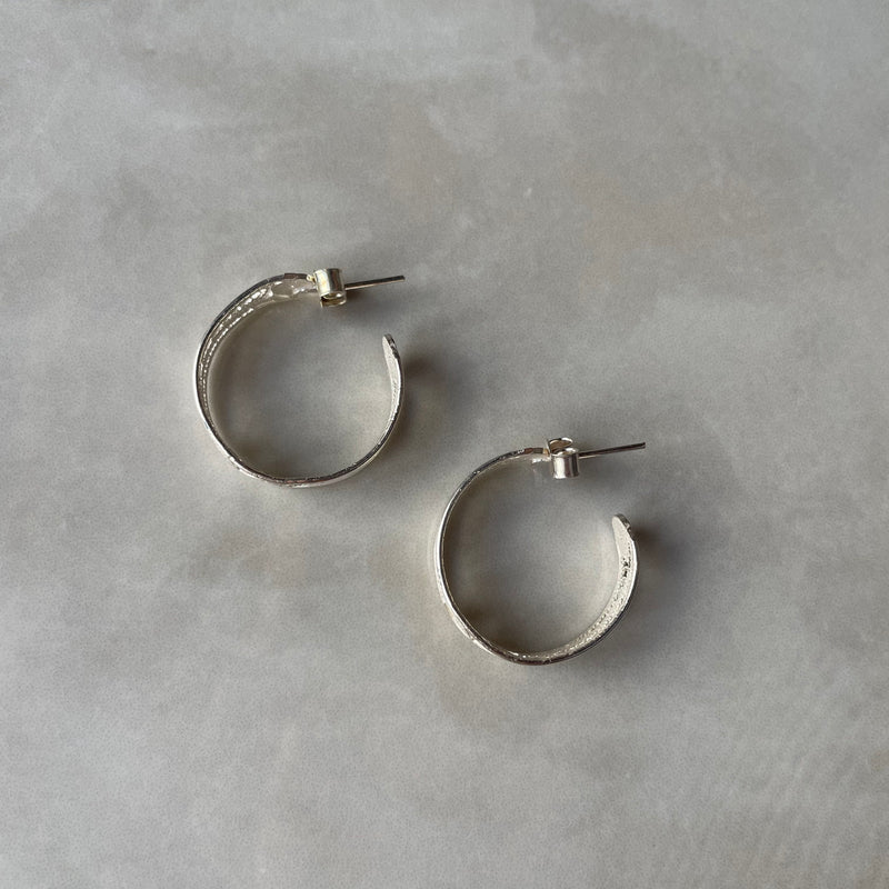 Silver hoop earrings on a grey textured surface | Deheb Jewellery Malta