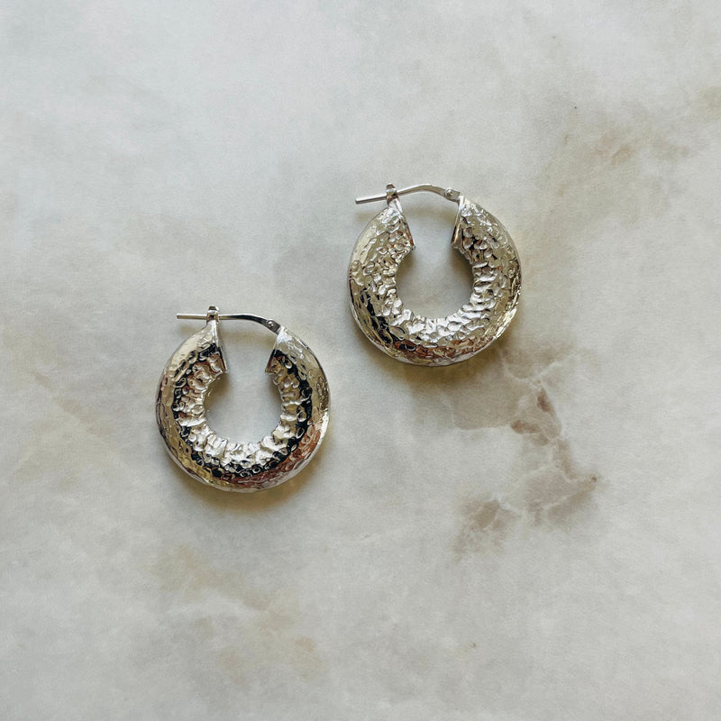 Pair of silver hoop earrings on a marble surface | Deheb Malta Jewellery 