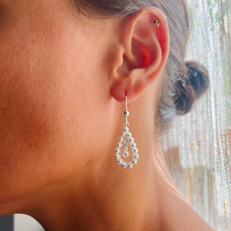 Close-up of a person wearing a silver teardrop earring with a blurred background