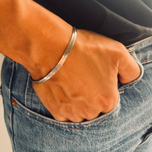 Hand wearing a silver bracelet with denim jeans in the background