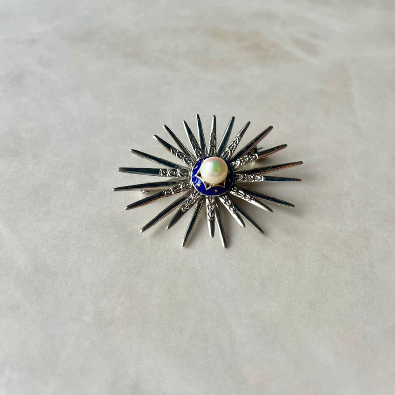 A star-shaped brooch made of 18 carat white gold, with a central cultivated pearl and blue enamel detail at the center.