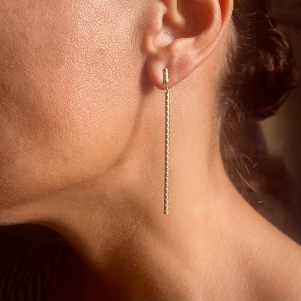 Close-up of an ear wearing a gold chain earring with a blurred background