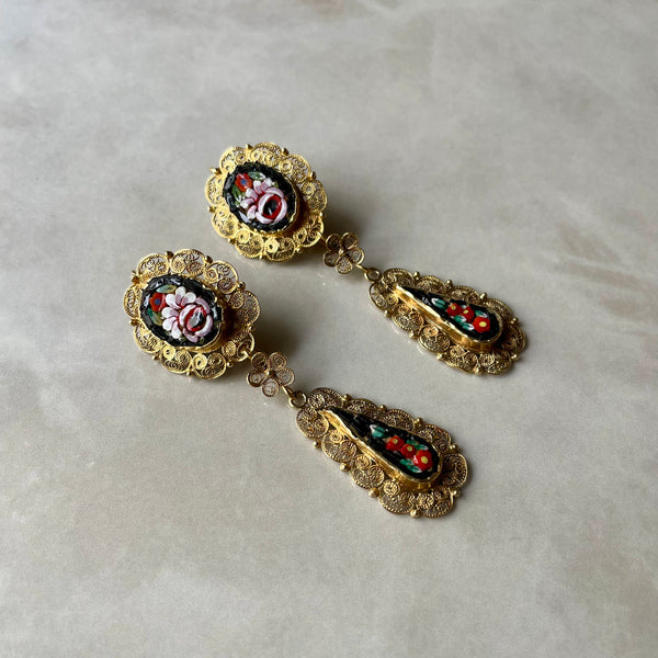 A pair of intricate gold filigree earrings with micro mosaic details, placed on a marble surface.