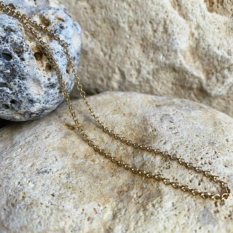 A gold-colored circular link chain necklace displayed against a natural stone background.